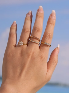 Detail of four gold-plated rings with colorful zircons worn on hand against a blue sky