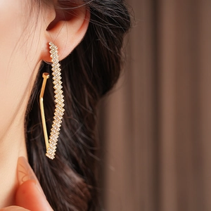 Dettaglio di eleganti orecchini geometrici in oro con diamanti luccicanti indossati da una modella