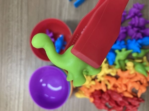 Detailed view of red tweezers picking up a colorful dinosaur toy for motor skill training