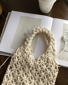 Detail of hand-woven off-white cotton handbag on a dark wood table with a cup of coffee
