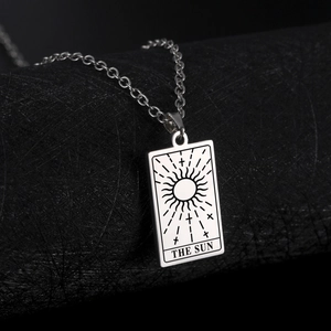 Macro shot of silver tarot card pendant with The Sun design on a black pedestal