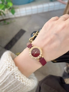 Elegant gold watch with burgundy leather strap worn on wrist against a white sweater