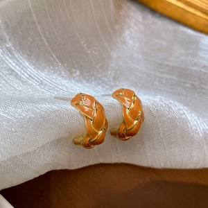 Nahaufnahme der orangefarbenen Emaille-Ohrringe mit goldener Webstruktur auf Stoff