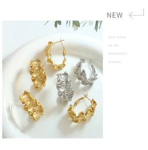 Détail de boucles d'oreilles froissées or et argent sur une assiette en porcelaine blanche