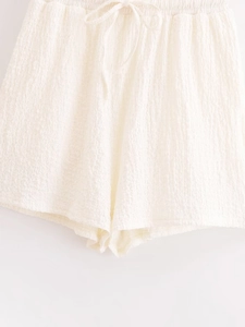 Detailed view of white textured shorts featuring elastic waistband and drawstring tie