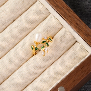 Detail of adjustable gold pearl ring with green enamel leaves and sparkling zircon