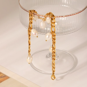 Detail of 18K gold plated Figaro anklet with baroque pearls hanging on a glass cup
