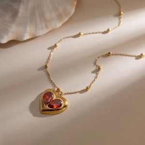Détail du pendentif cœur doré avec zircons rouges et chaîne à billes sous lumière