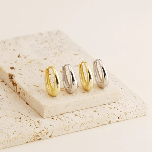 Detailed close-up of gold and silver U-shaped hoop earrings on a beige travertine stone