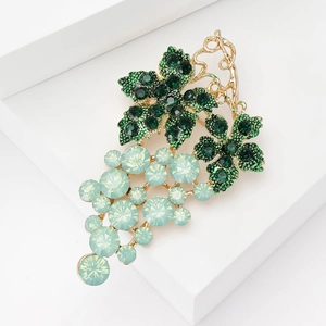 Macro shot of gold grape brooch with green and blue crystals on white stand
