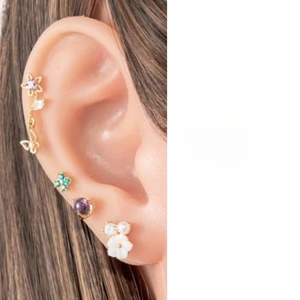 Close-up of ear piercing set with butterfly zircon and clover earrings on a model