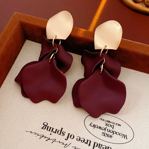 Macro detail of irregular gold floral earrings with crimson resin petals on a display box