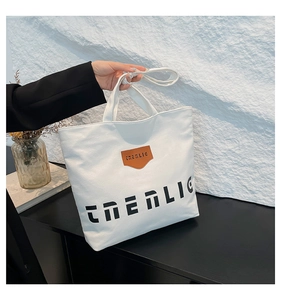 Close-up of white canvas tote with brown leather logo patch and black CNERLIG print