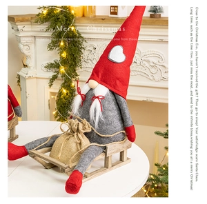 Close-up of a Christmas gnome with red heart hat, wooden sled and burlap gift bag decor