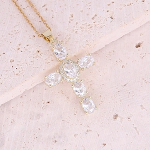 Dettaglio della collana in rame dorato con ciondolo a croce in zircone su pietra beige