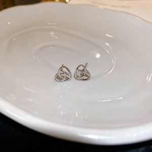 Macro shot of silver woven knot earrings on a white ceramic tray with polished finish
