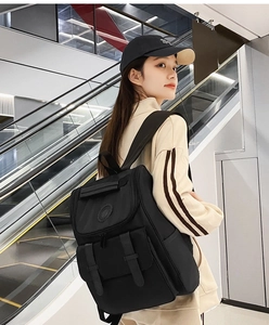 Lifestyle shot of a black flap backpack with dual buckle straps worn on an escalator