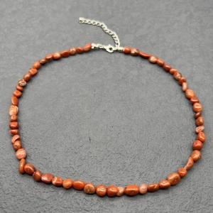 Macro detail of natural red stone beads on a stainless steel necklace with lobster clasp