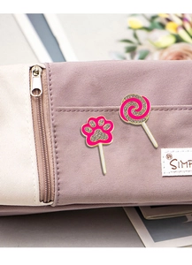 Close-up of pink enamel cat paw and lollipop pins with crystals on a canvas bag