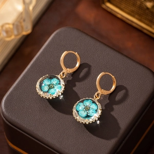 Macro detail of golden earrings with clear glass ball containing a blue dried flower