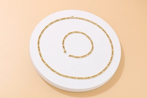 Detailed view of golden Figaro chain necklace and bracelet set on a white display pedestal