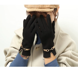 Detail of black thermal gloves featuring a gold chain buckle and elegant wavy cuffs