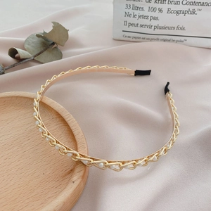 Detail of gold chain headband woven with white pearls on a soft pink background