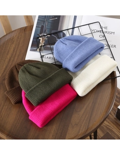 Close-up of colorful knitted beanies in five solid colors on a wooden surface