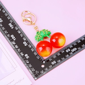 Close-up of red and yellow gradient cherry keychain with green rhinestones on scale