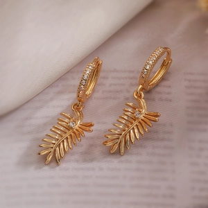 Elegant gold leaf earrings with sparkling zircon accents on a soft fabric background