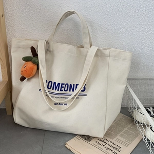 Detail of a large canvas tote bag in creamy white with a decorative orange persimmon charm