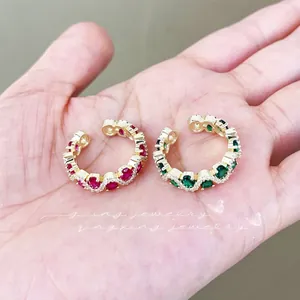 Macro detail of gold-plated ear cuffs with red and green stones and pavé zircon