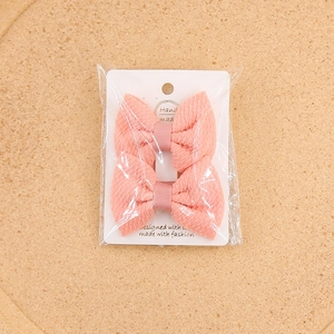 Detail of pink peach bow hair clips with ripple texture on white card in polybag packaging
