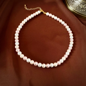 Détail du collier de perles roses et blanches avec fermoir doré sur soie marron