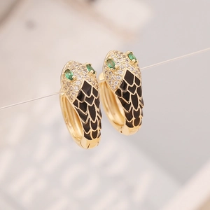 Macro shot of gold snake-head earrings with green eyes and black enamel detail