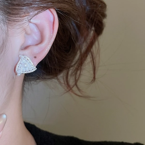Detail view of triangular pearl stud earrings with sparkling zircons on a model's ear
