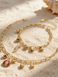 Détail d'un bracelet double couche plaqué or 18k avec breloques coccinelle et cœur sur sable