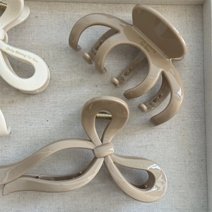Close-up of three glossy hair claws in cream and beige with gold engraved text detail