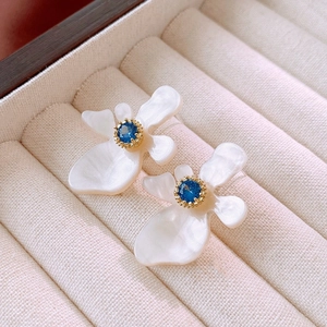 Detailed macro view of white flower earrings with blue zircon and golden center detail