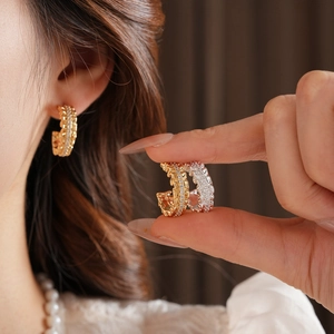 Detailed view of C-shaped woven gold and silver earrings with sparkling diamond inlay