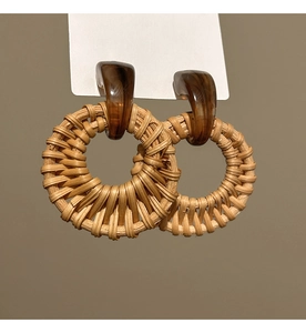 Macro detail of natural rattan woven hoop earrings with brown resin stud on white card