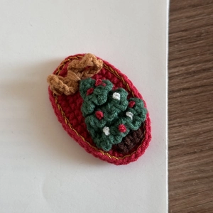 Detail of handmade knit Christmas tree hair clip with red base and golden border decor