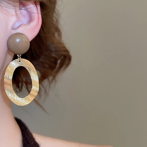 Detailed close-up of a brushed gold oval hoop earring with a dark brown resin stud top