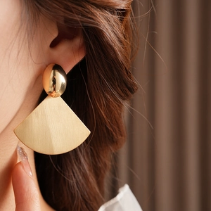 Close-up of golden oval brushed fan earrings featuring a matte texture and polished stud