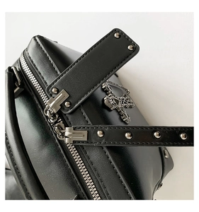 Close-up of black leather bag with silver studs, metal zippers and cross pendant