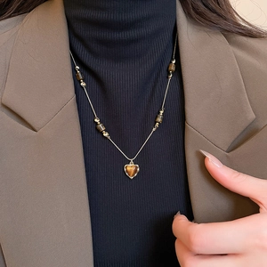 Detail of heart-shaped tiger eye stone pendant on a gold beaded chain worn over a suit