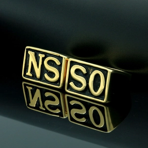 Macro shot of gold square signet ring with embossed letters on a reflective surface