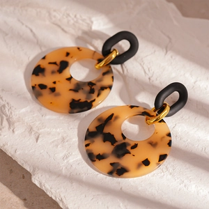 Detail of leopard print resin hoop earrings with gold links on a white stone background