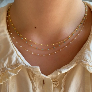 Détail de colliers dorés en acier inoxydable avec des perles en émail colorées