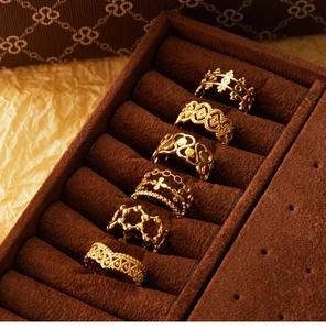 Detail view of six 18K gold plated hollow floral rings arranged in a brown velvet jewelry box